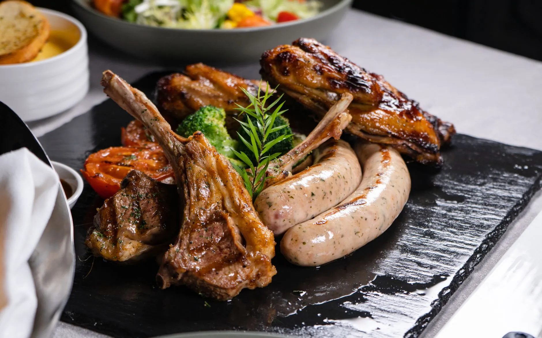 Costillas de cordero con salchichas y verduras sobre una pizarra