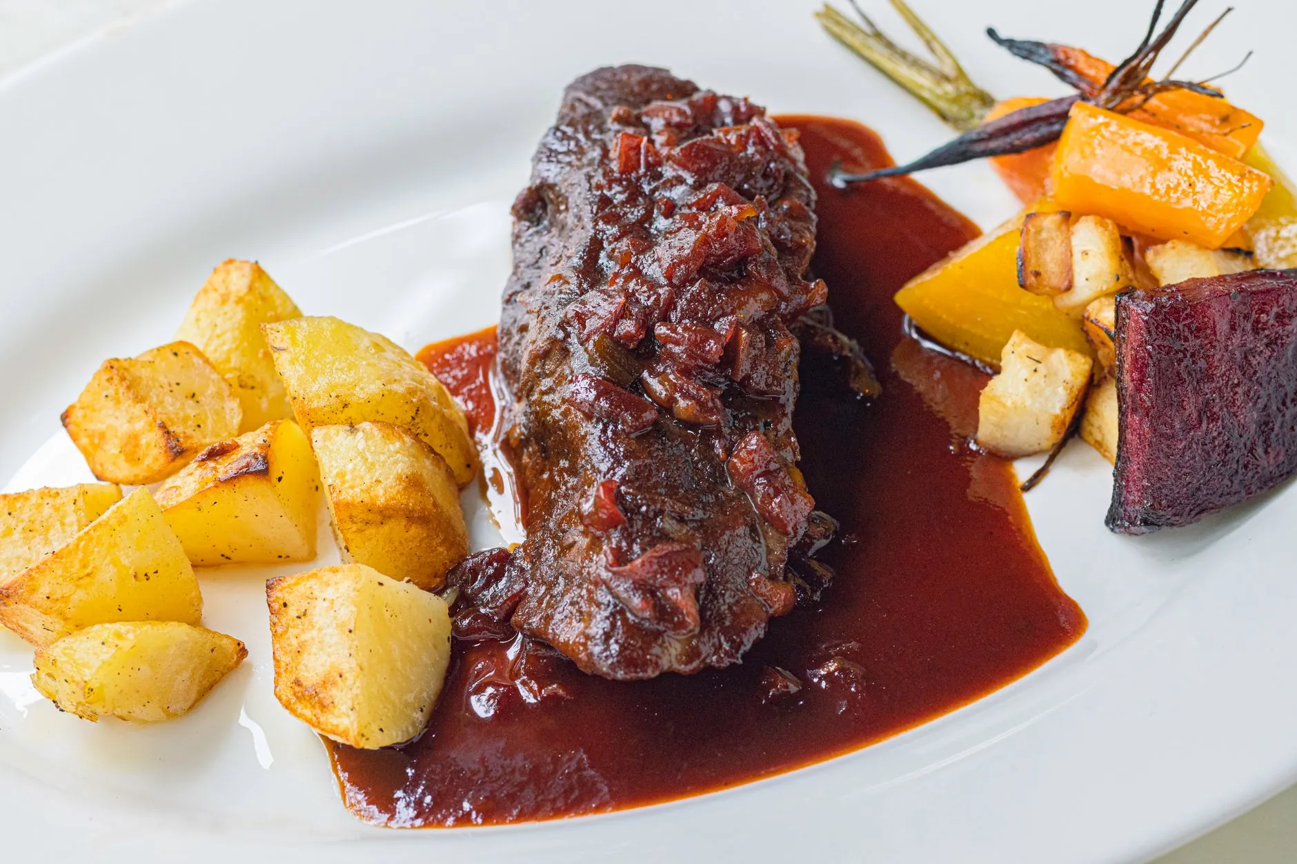 Corte de carne con papas asadas y salsa sobre un plato blanco